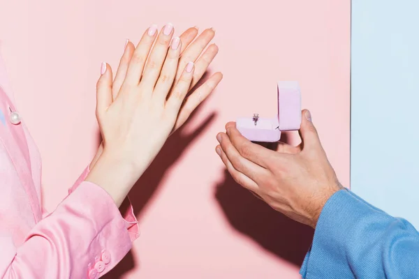 Abgeschnittene Ansicht eines Mannes, der einer klatschenden Frau einen Heiratsantrag auf rosa und blauem Hintergrund macht — Stockfoto