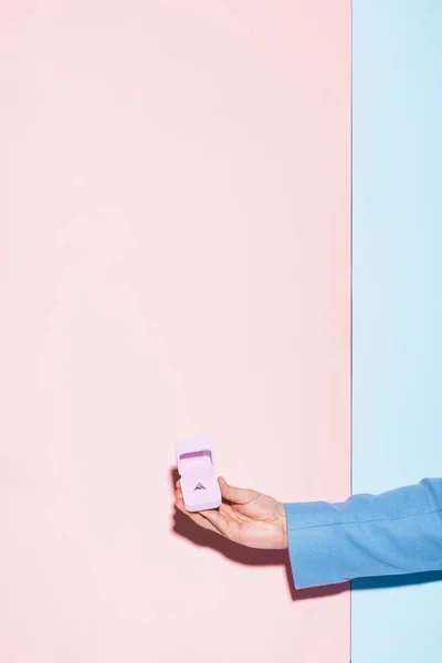 Vista recortada de la caja de espera del hombre con anillo de compromiso sobre fondo azul y rosa - foto de stock