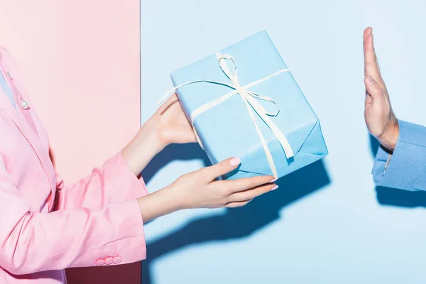 Vista recortada de la mujer dando regalo al hombre sobre fondo rosa y azul - foto de stock