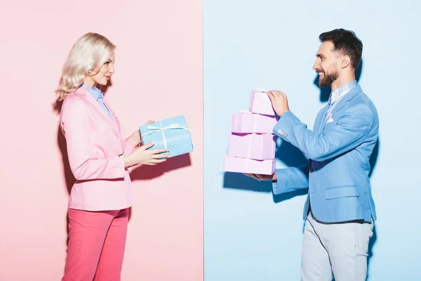 Vista laterale di donna attraente e uomo sorridente che tiene regali su sfondo rosa e blu — Foto stock