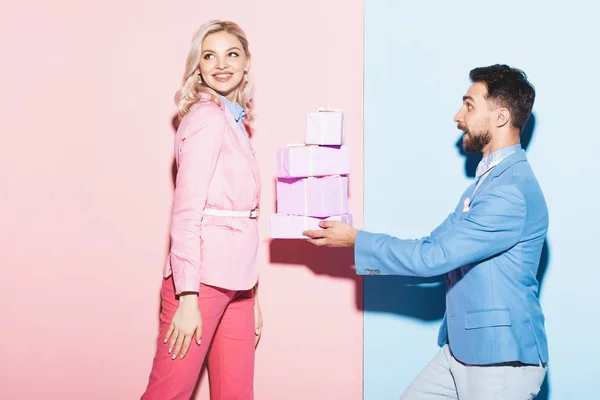 Bell'uomo che fa regali alla donna sorridente su sfondo rosa e blu — Foto stock