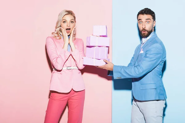 Hombre guapo dando regalos a la mujer conmocionada sobre fondo rosa y azul — Stock Photo