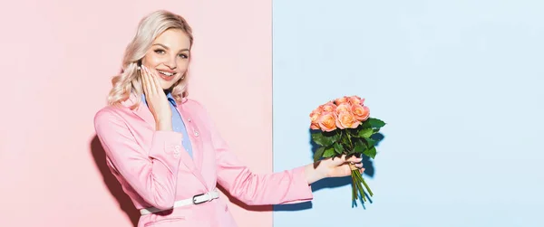 Panoramaaufnahme einer lächelnden Frau mit Blumenstrauß auf rosa und blauem Hintergrund — Stockfoto