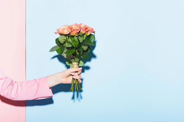 Vista recortada de la mujer sosteniendo ramo sobre fondo rosa y azul - foto de stock