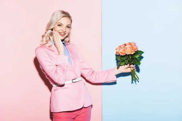 Lächelnde Frau mit Blumenstrauß auf rosa und blauem Hintergrund — Stockfoto