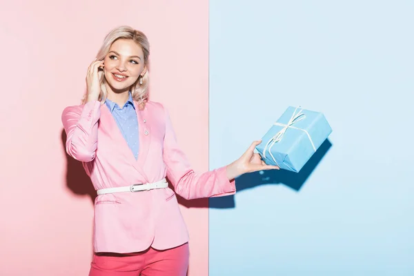 Mulher sorridente segurando caixa de presente no fundo rosa e azul — Fotografia de Stock