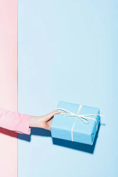 Vista recortada de la mujer sosteniendo caja de regalo sobre fondo rosa y azul - foto de stock