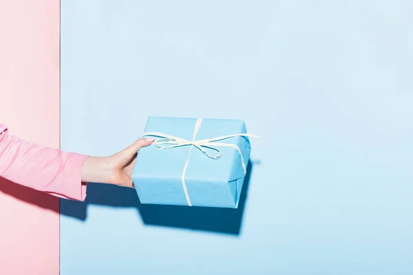 Cropped view of woman holding gift box on pink and blue background — Stock Photo