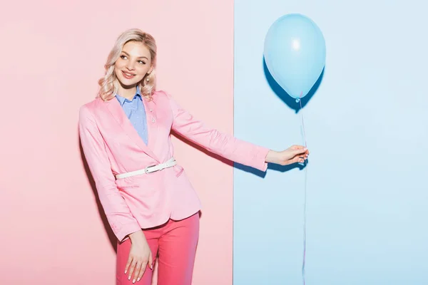 Улыбающаяся женщина держит воздушный шар на розовом и синем фоне — стоковое фото