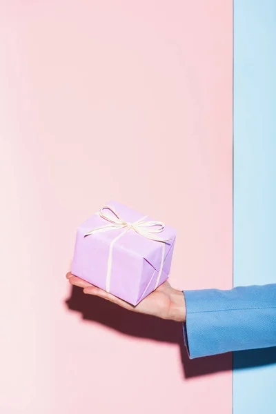 Vista recortada del hombre sosteniendo regalo sobre fondo azul y rosa - foto de stock