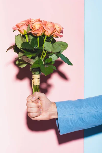 Обрезанный вид человека, держащего букет на синем и розовом фоне — стоковое фото