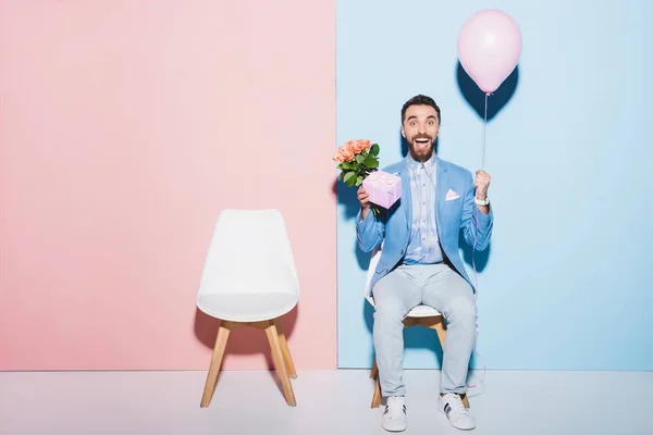 Uomo bello e sorridente che tiene palloncino, regalo e su sfondo blu e rosa bouquet — Foto stock