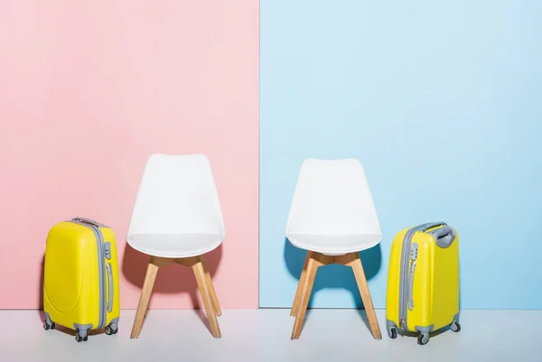 Sillas de madera y bolsas de viaje sobre fondo rosa y azul - foto de stock