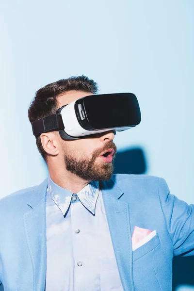 Hombre sorprendido en los auriculares de realidad virtual sobre fondo azul - foto de stock