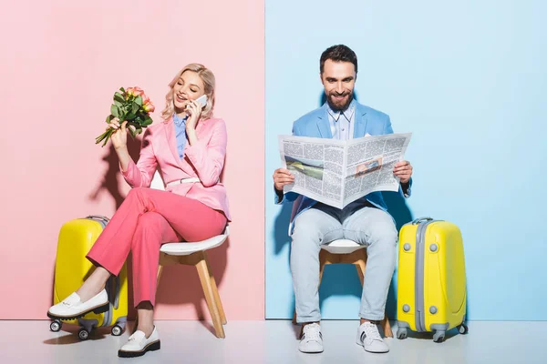Attractive woman talking on smartphone and smiling man reading newspaper on pink and blue background — Stock Photo