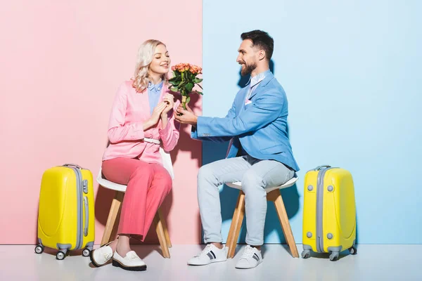 Schöner Mann überreicht lächelnden Frau Blumenstrauß auf rosa und blauem Hintergrund — Stockfoto