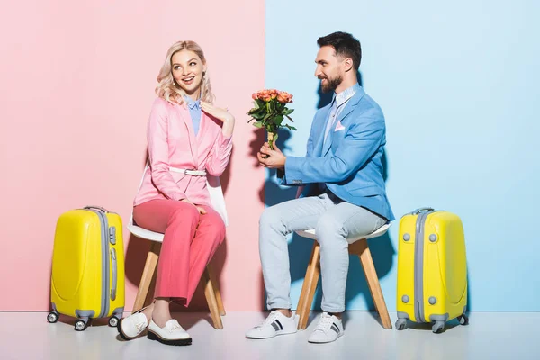 Hombre guapo dando ramo a la mujer conmocionada sobre fondo rosa y azul - foto de stock