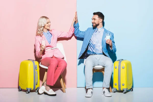 Sonriente mujer y guapo hombre mostrando alta cinco y la celebración de cócteles en rosa y azul fondo - foto de stock