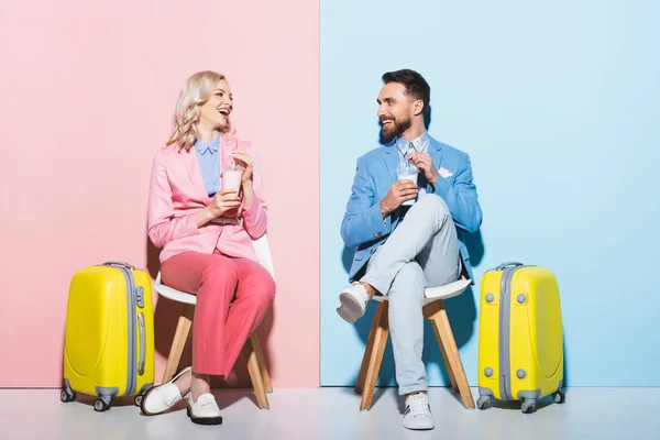Улыбающаяся женщина и красивый мужчина с коктейлями на розовом и синем фоне — стоковое фото