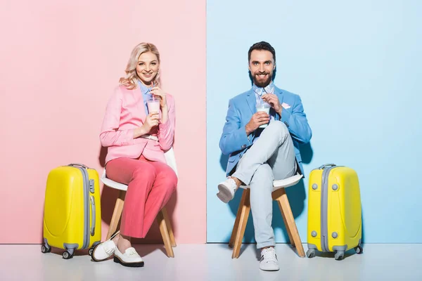 Mujer sonriente y hombre guapo sosteniendo cócteles sobre fondo rosa y azul - foto de stock