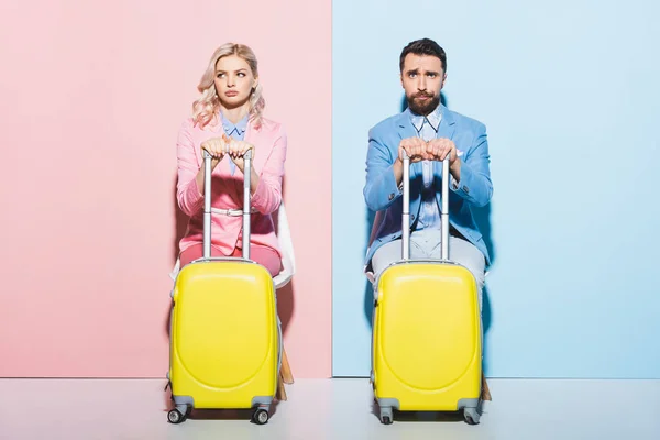 Traurige Frau und schöner Mann mit Reisetaschen auf rosa und blauem Hintergrund — Stockfoto
