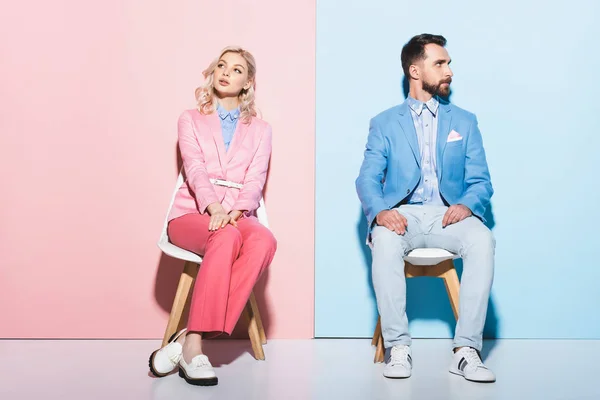 Dreamy woman and handsome man sitting on chairs on pink and blue background — Stock Photo