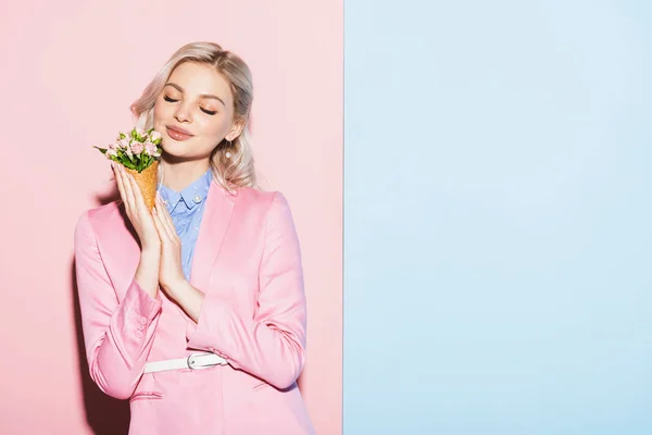 Mujer sonriente con los ojos cerrados sosteniendo ramo sobre fondo rosa y azul - foto de stock