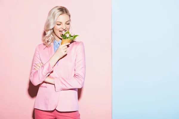 Mujer sonriente comiendo ramo sobre fondo rosa y azul - foto de stock