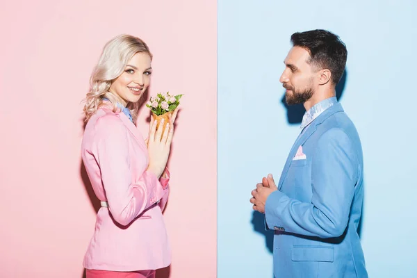 Vista lateral de la mujer sonriente con ramo y hombre guapo sobre fondo rosa y azul — Stock Photo