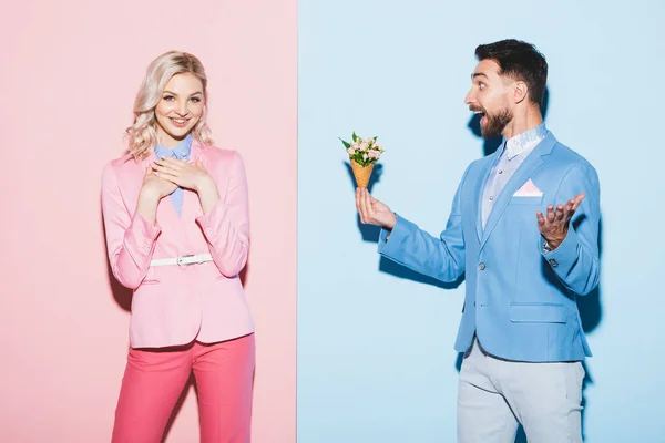 Homme choqué donnant bouquet à la femme attrayante sur fond rose et bleu — Photo de stock