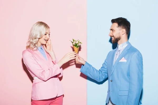 Lächelnder Mann überreicht schockierten Frauen Blumenstrauß auf rosa und blauem Hintergrund — Stockfoto