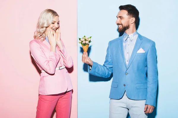 Smiling man giving bouquet to shocked woman on pink and blue background — Stock Photo