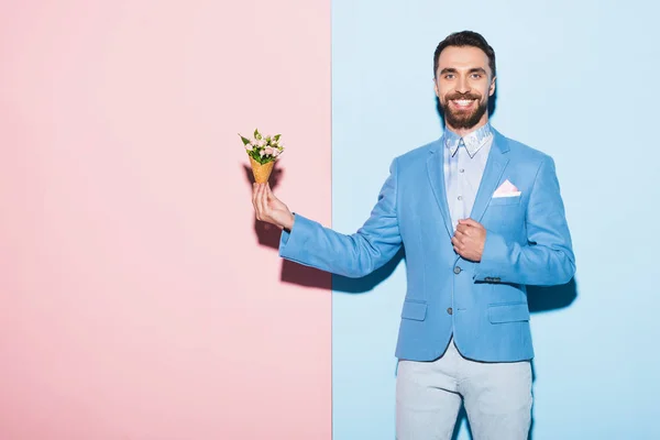 Smiling man holding bouquet on pink and blue background — Stock Photo