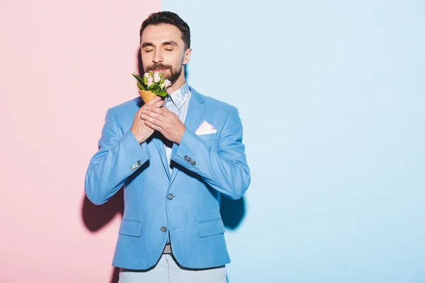 Smiling man smelling bouquet on pink and blue background — Stock Photo