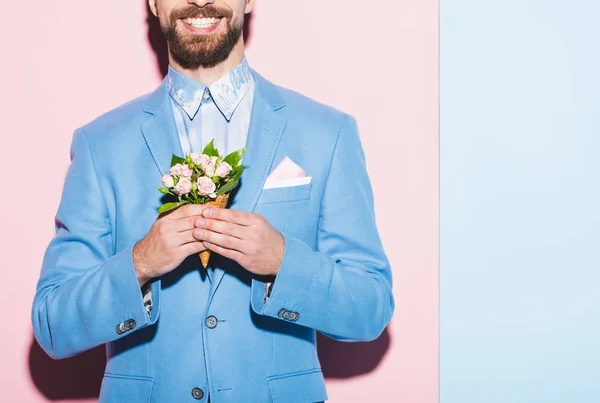 Vue recadrée de l'homme souriant tenant bouquet sur fond rose et bleu — Photo de stock