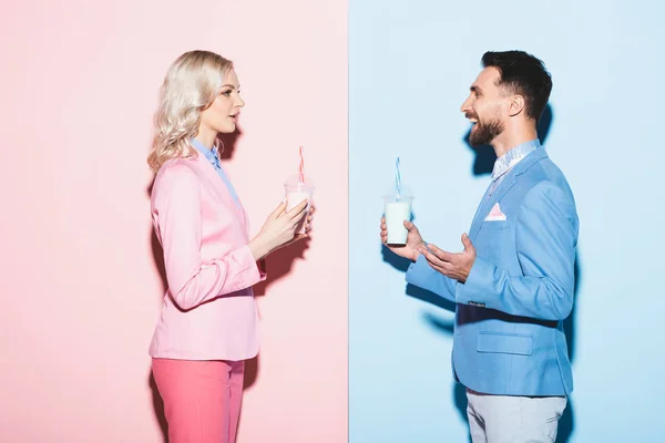 Seitenansicht attraktiver Frau und lächelndem Mann mit Cocktails auf rosa und blauem Hintergrund — Stockfoto