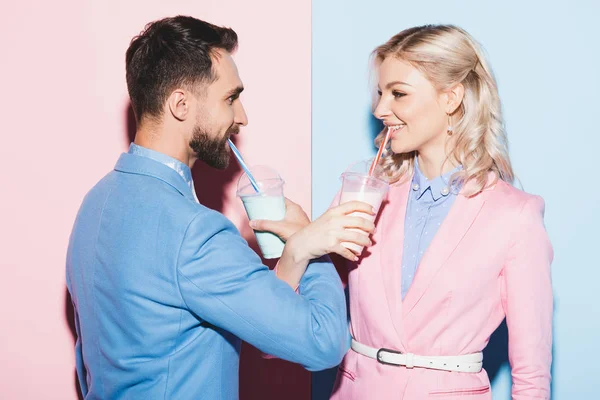 Attraktive Frau und lächelnder Mann, die Cocktails auf rosa und blauem Hintergrund trinken — Stockfoto