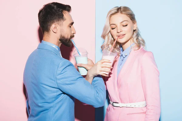 Femme souriante et homme buvant des cocktails sur fond rose et bleu — Photo de stock