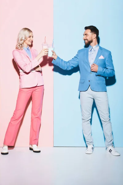 Smiling woman and man clinking with cocktails on pink and blue background — Stock Photo