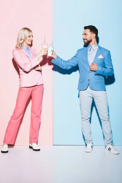 Mulher sorridente e homem clinking com coquetéis em fundo rosa e azul — Fotografia de Stock