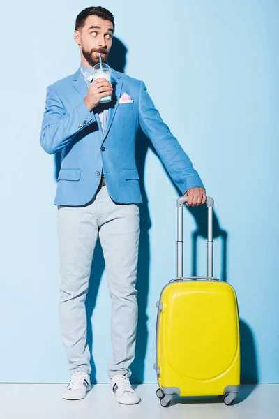 Homem bebendo coquetel e segurando saco de viagem no fundo azul — Fotografia de Stock