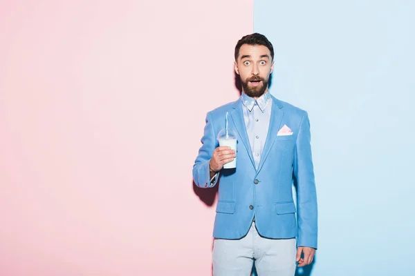 Шокированный мужчина держит коктейль на розовом и синем фоне — стоковое фото