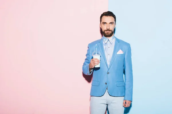 Серьезный человек держит коктейль на розовом и синем фоне — стоковое фото