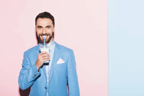 Smiling man drinking cocktail on pink and blue background — Stock Photo