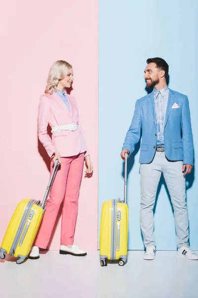 Femme souriante et bel homme avec des sacs de voyage sur fond rose et bleu — Photo de stock