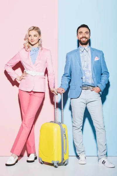 Mulher sorridente e homem bonito com saco de viagem em fundo rosa e azul — Fotografia de Stock