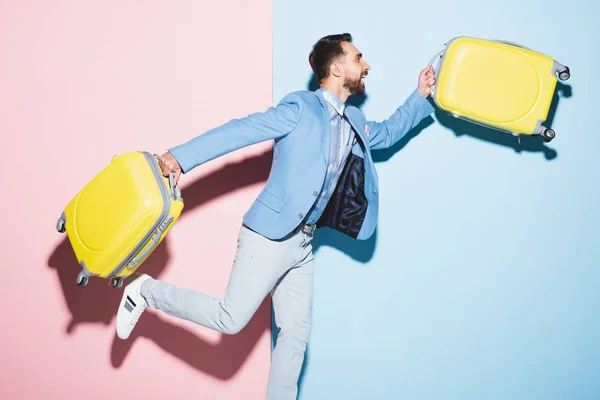 Sonriente hombre sosteniendo bolsas de viaje sobre fondo rosa y azul - foto de stock