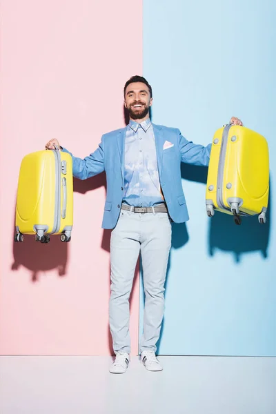 Uomo sorridente che tiene borse da viaggio su sfondo rosa e blu — Foto stock