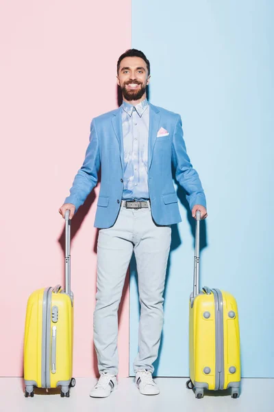 Homem sorridente segurando sacos de viagem em fundo rosa e azul — Fotografia de Stock