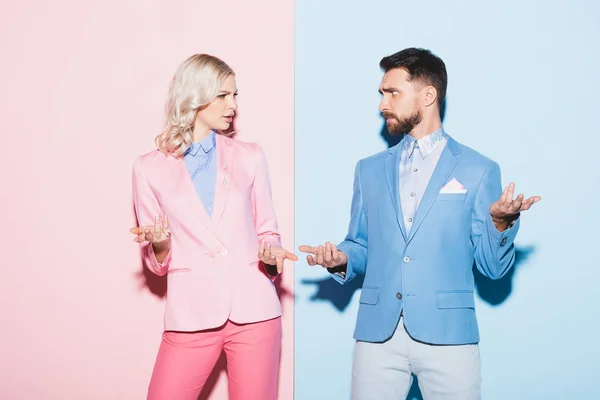 Irritated woman and handsome man looking at each other on pink and blue background — Stock Photo